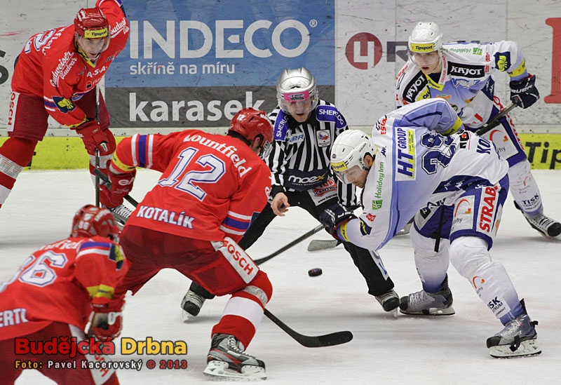 Čárový rozhodčí Skopal háže puk mezi hokejky Kotalíka a Koreise