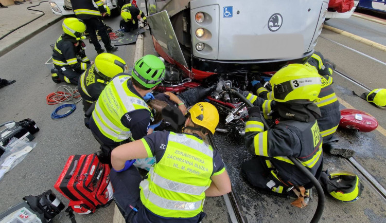Motorkář skončil zaklíněný pod tramvají. Při vědomí ho vyprošťovali hasiči