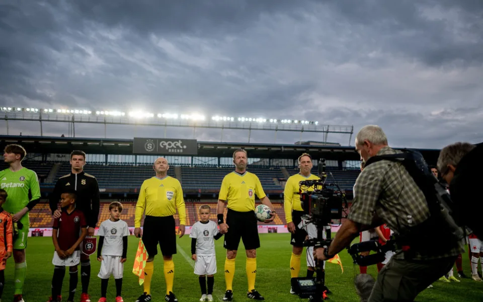 Režisér Kolečko točí film na letenském stadionu, hledá stovky sparťanských komparsistů. Dostanou jídlo a dárek